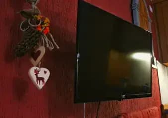 Televisione appesa al muro vicino al divano, con al suo lato una decorazione con cuori