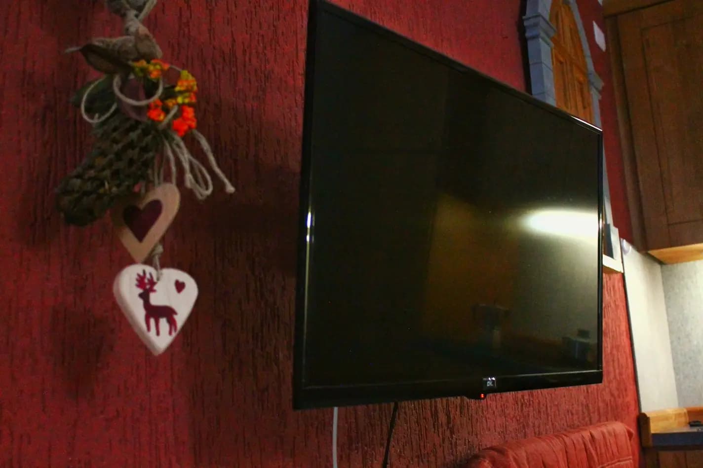 Televisione appesa al muro vicino al divano, con al suo lato una decorazione con cuori